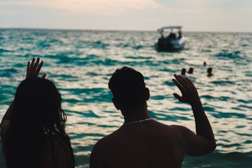 Two people facing the ocean with a boat and swimmers in the distance. 5