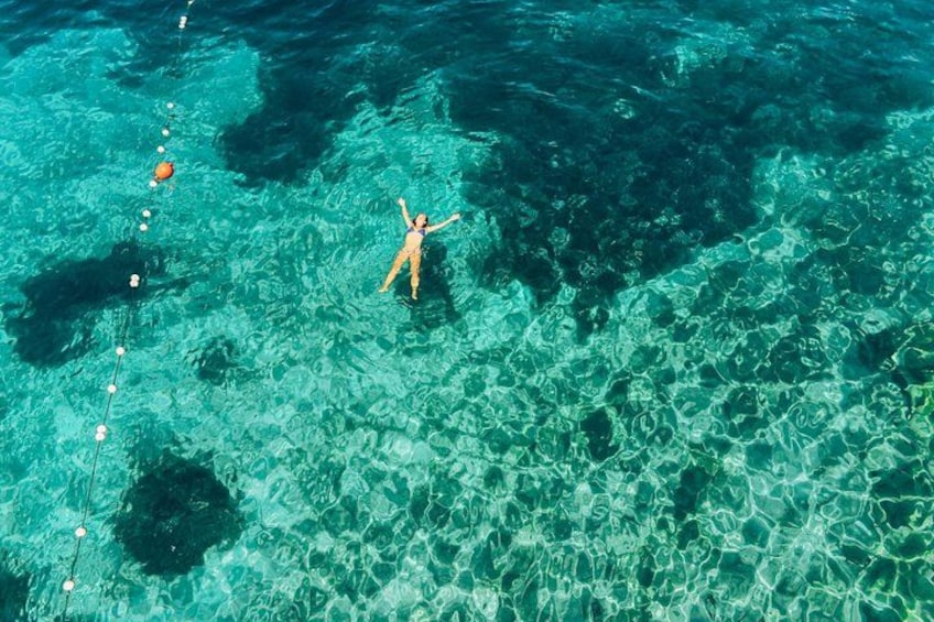 A person floating on clear turquoise water with a coral reef in the background. 3
