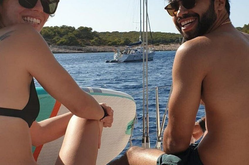 A couple on a boat with a sail, water, and a distant shoreline with trees. 4