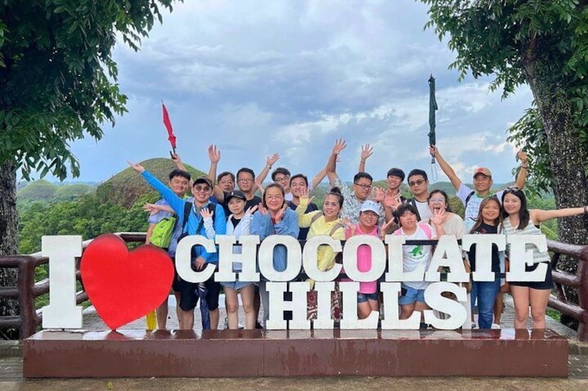 En gruppe mennesker poserer foran et skilt med teksten 'I ♥ CHOCOLATE HILLS'. 1