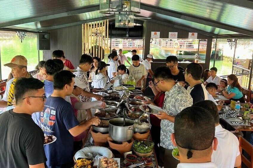 A group of people gathered around a long table with various food items and cooking equipment. 2
