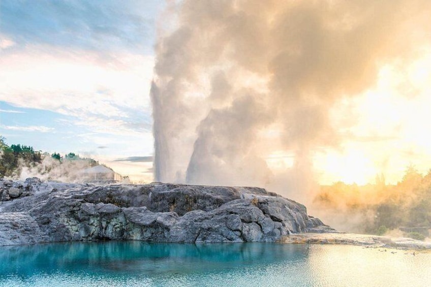 A geyser with a large plume of steam, a turquoise pool, and a rocky landscape. 1
