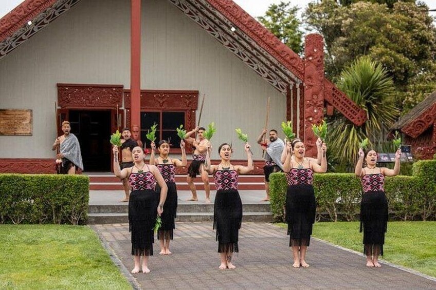 A group of people in traditional attire standing in front of a building with a red roof and white walls. 3