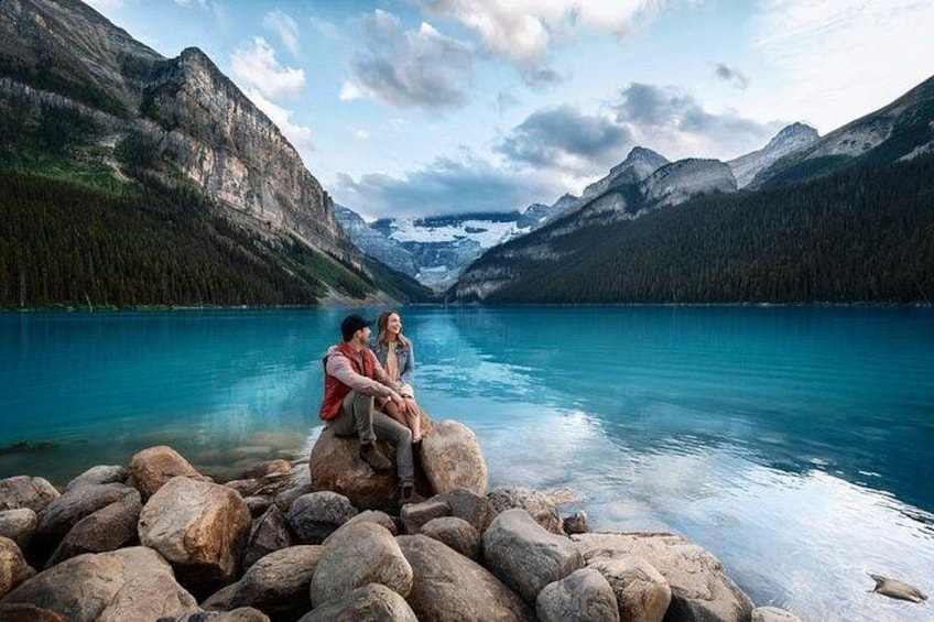 A couple sitting on rocks by a lake with mountains in the background. 3
