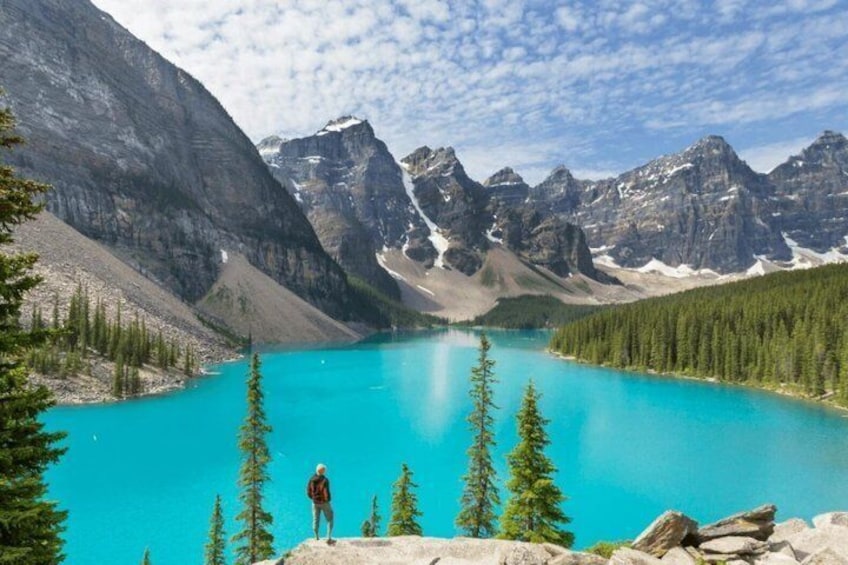 Una persona de pie sobre una roca, contemplando un lago turquesa rodeado de montañas. 2