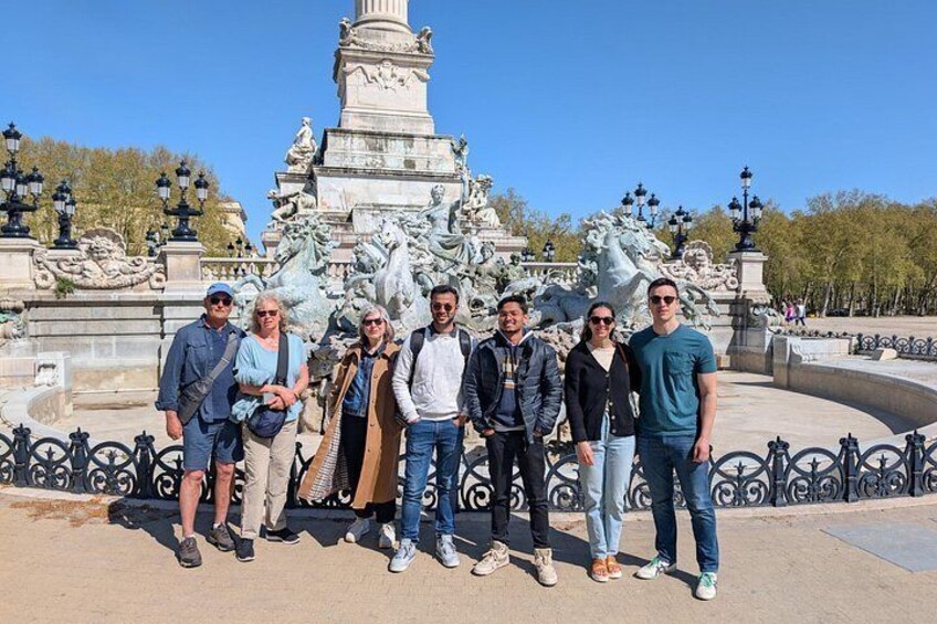 A group of people standing in front of a large fountain with statues and a monument in the background. 1