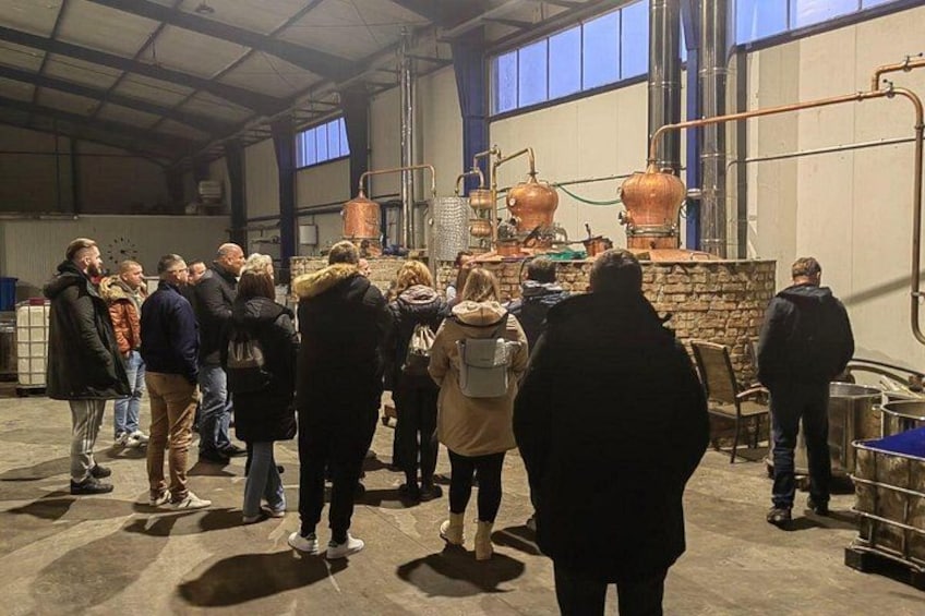 En gruppe mennesker der ser på industrimaskiner, herunder kobberkedler, i en stor indendørs bygning. 1