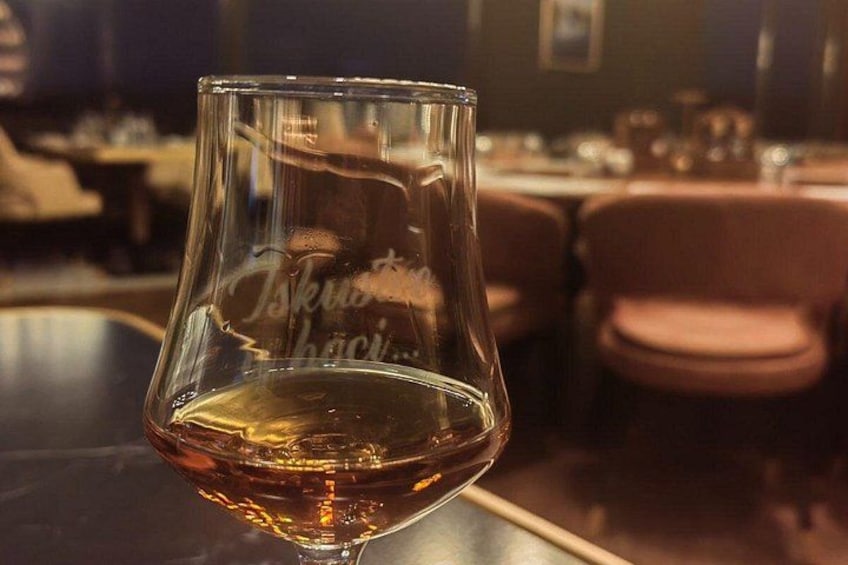 Et glas med gyldent væske, med en spejllignende overflade, stående på et bord i et svagt oplyst rum. 3