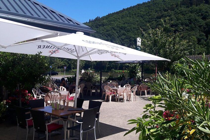 Ein Essbereich im Freien mit Tischen und Stühlen unter Sonnenschirmen, umgeben von Grünflächen und einer hügeligen Landschaft. 2