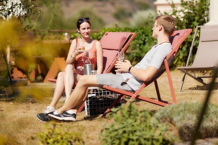 Two people sitting on red lounge chairs outdoors, one holding a drink. 5