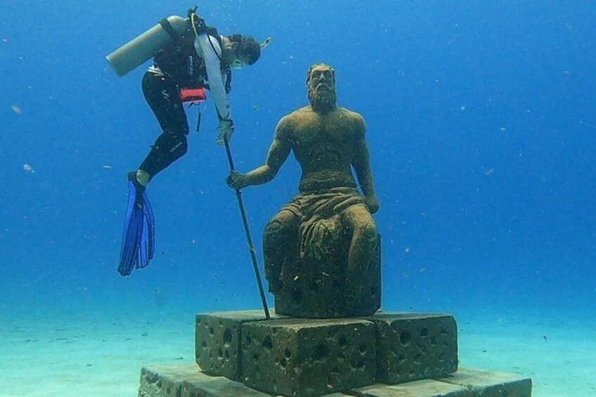 A diver with a scuba tank and fins interacting with a stone statue underwater. 1