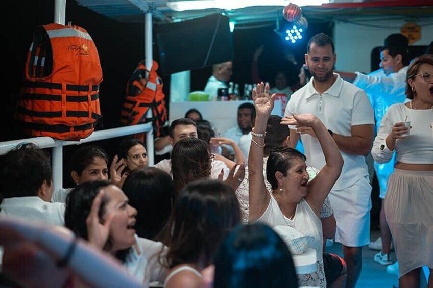 A group of people in a social gathering, some raising their hands, with a person in the foreground wearing a white shirt. 5