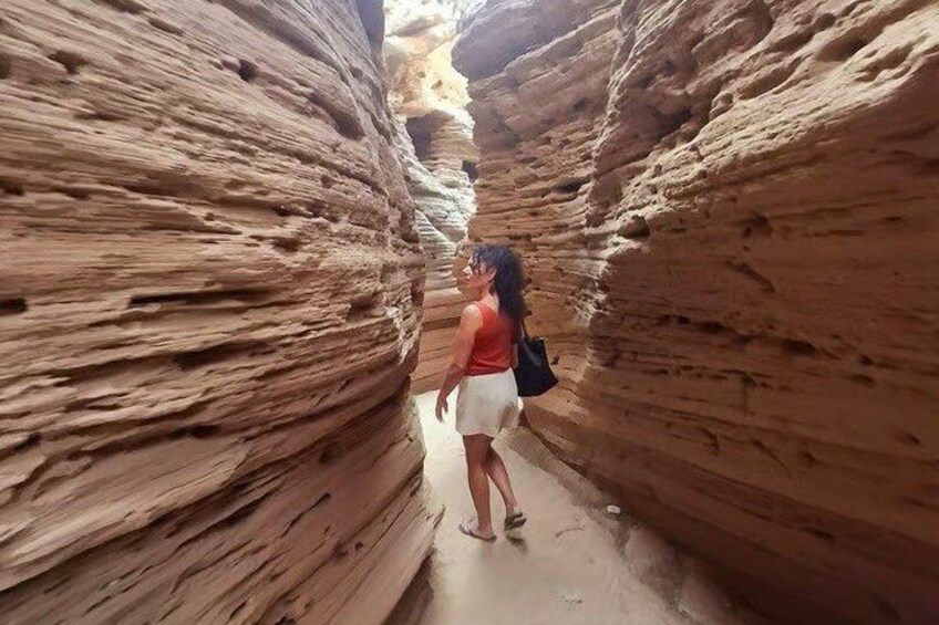 A person standing in a narrow canyon with layered rock formations. 2