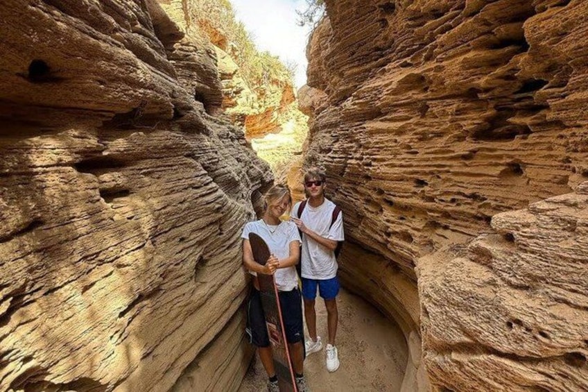 Two people standing in a narrow canyon with layered rock formations. 4