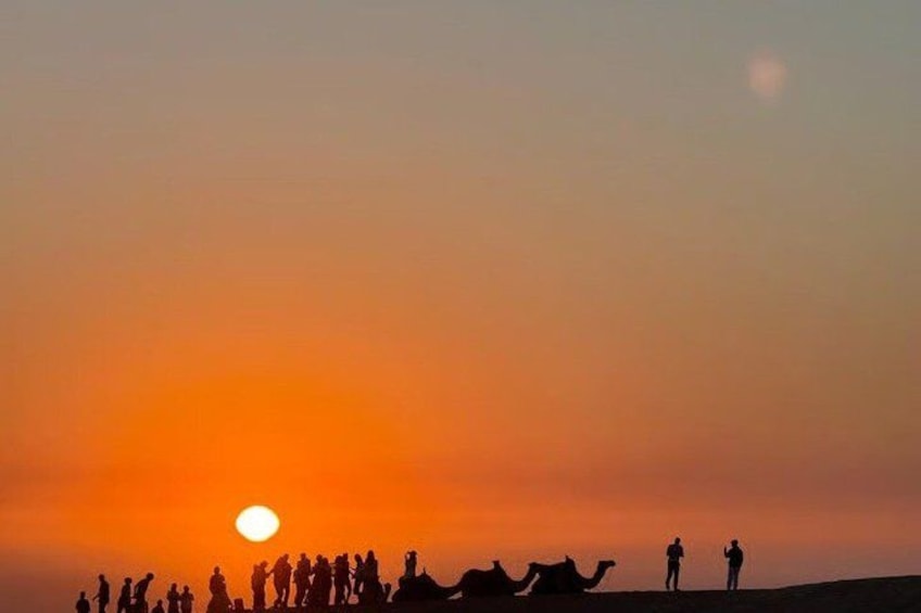 A sunset with silhouettes of people and camels on a desert landscape. 3