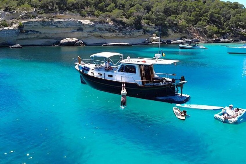A boat anchored in turquoise waters with a rocky coastline in the background. 1