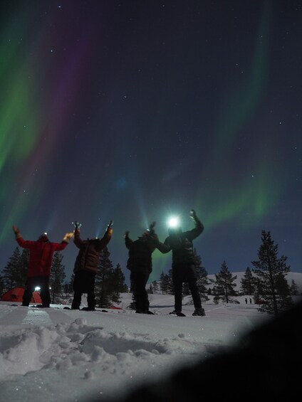 Four people celebrating under the Northern Lights in a snowy landscape. 5