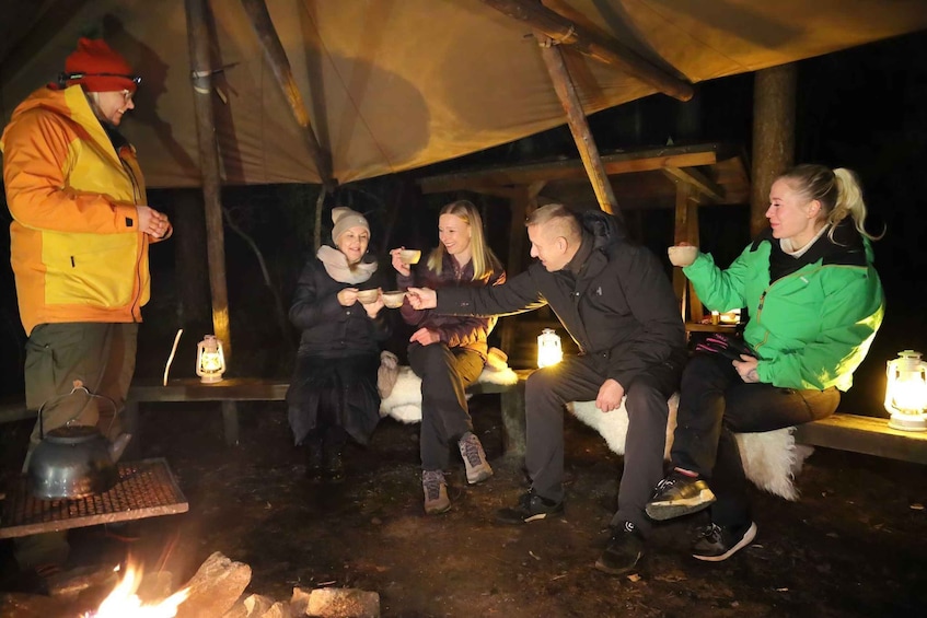 A group of people sitting around a campfire in a tent. 2
