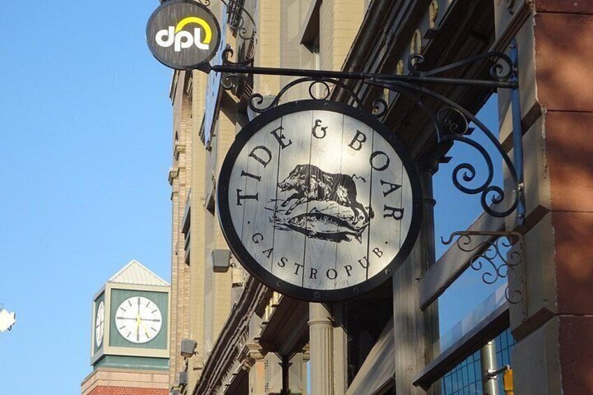A building with a sign for 'Tide & Boar Gastro Pub' and a clock tower in the background. 2