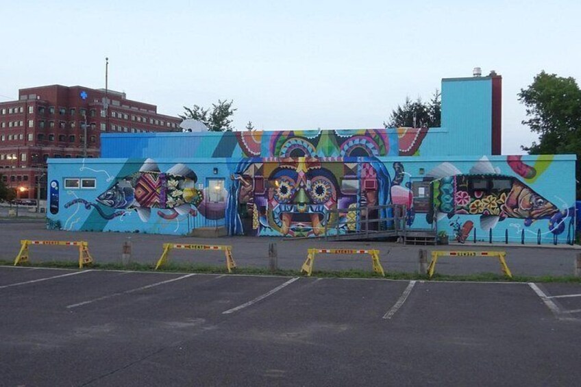 A colorful mural on a building, a parking lot, and a red building in the background. 5