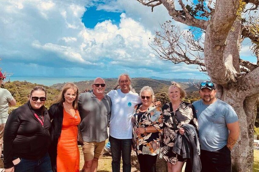 A group of people standing outdoors with a tree and a scenic landscape in the background. 3