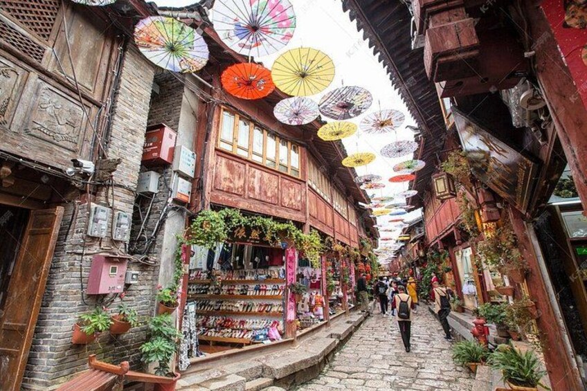 Una calle estrecha con edificios de madera, sombrillas coloridas y plantas en macetas. 5