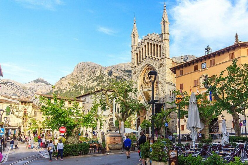 Une place animée, avec une église imposante, des passants et des terrasses. 2