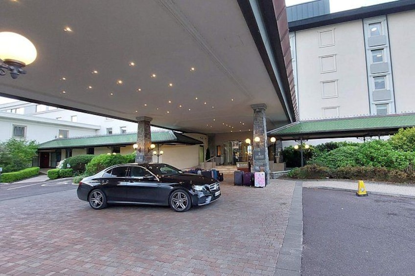 A black car parked under a covered area with a building in the background. 4