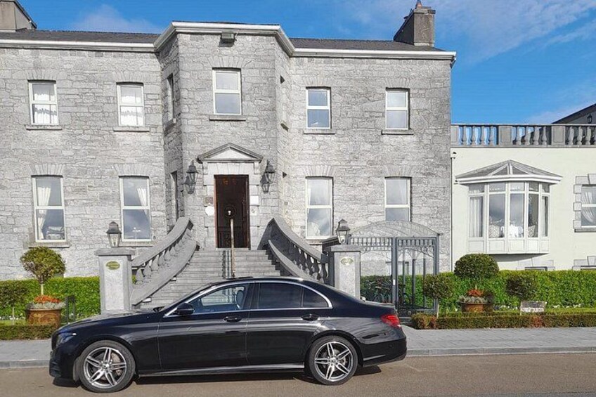 A black car parked in front of a stone building with a staircase leading to the entrance. 2