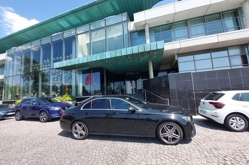 A modern building with large glass windows and a green roof. There are three cars parked in front. 5