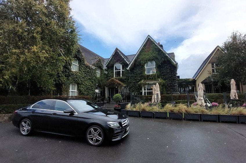 A black car parked in front of a house with ivy-covered walls and a garden with outdoor furniture. 3