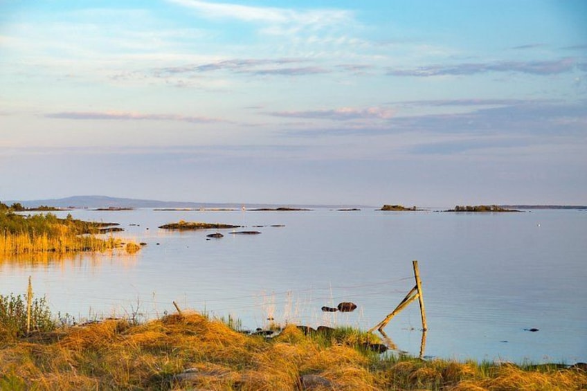 A calm lake with grassy banks, a wooden structure, and distant islands. 4