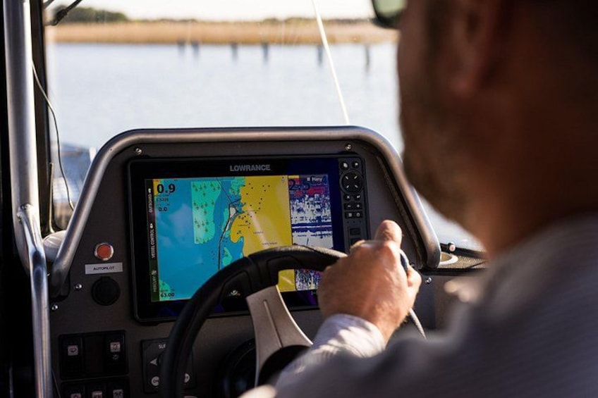 A person steering a boat with a navigation screen displaying a map and various controls. 4