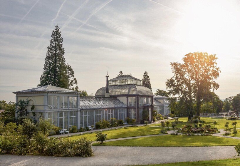 A large greenhouse with a glass dome and a smaller glass structure, surrounded by a well-maintained garden with trees and shrubs. 3