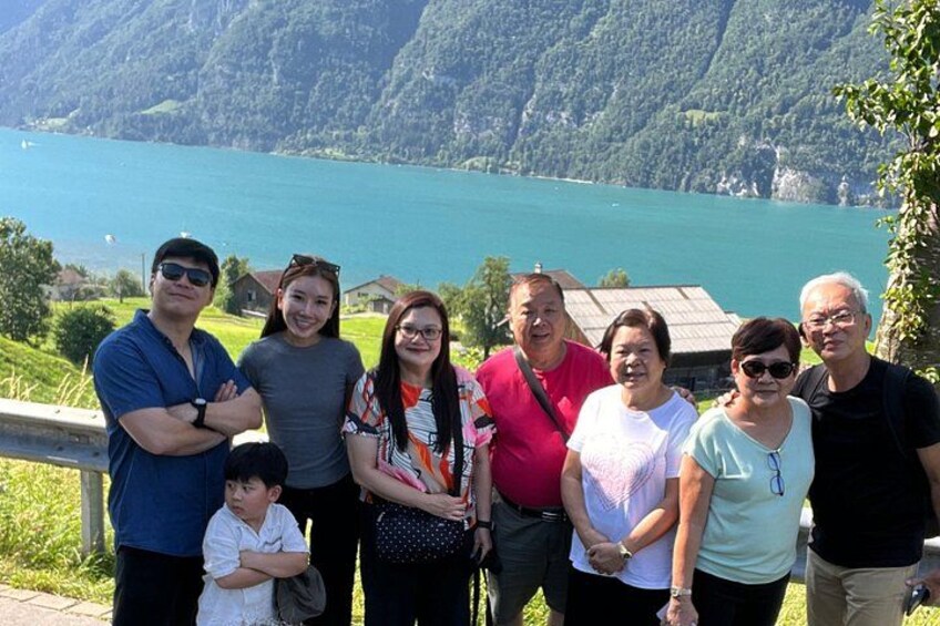 Un grupo de personas de pie junto a un lago, con montañas al fondo. 5