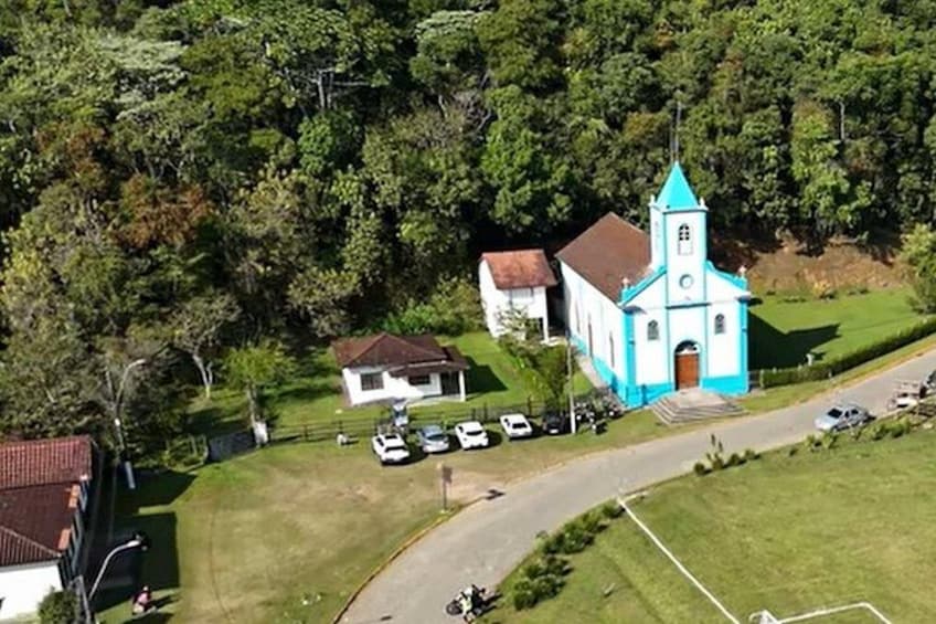 En kirke med et blåt tårn, omgivet af et grønt landskab og et par parkerede biler. 1