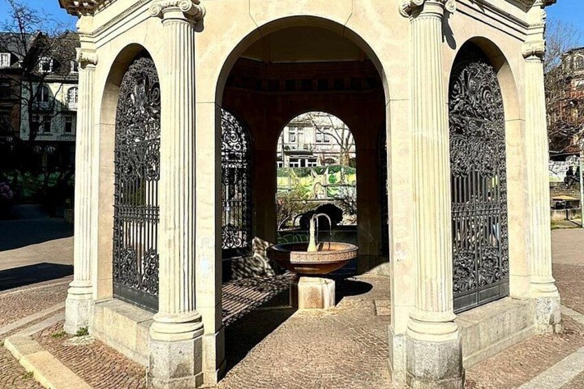 An ornate stone archway with intricate metalwork and a fountain at its base. 3