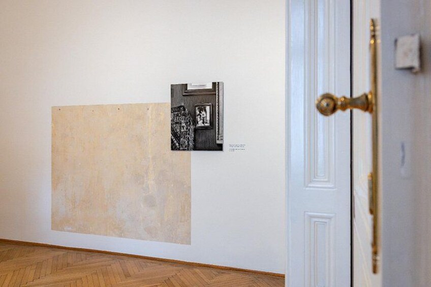 A room with a large abstract painting on the wall, a door with a brass handle, and a patterned wooden floor. 2