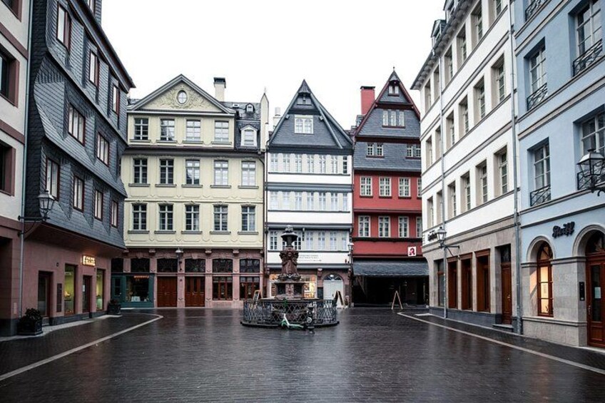Une place de style européen, avec des bâtiments historiques, une fontaine et un ciel dégagé. 1