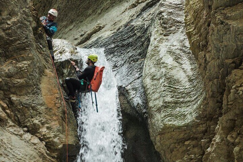 Two people rappelling down a waterfall in a rocky canyon. 3