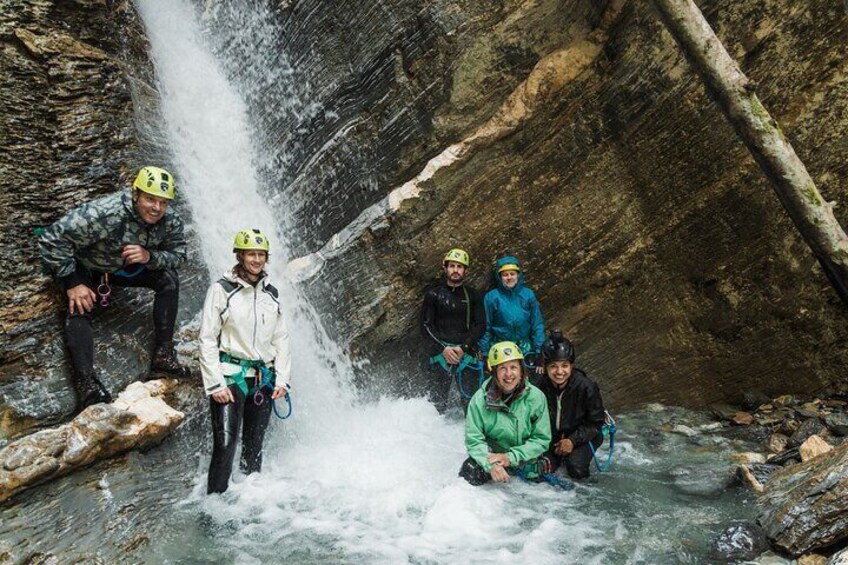 A group of people in helmets and harnesses near a waterfall in a rocky canyon. 2