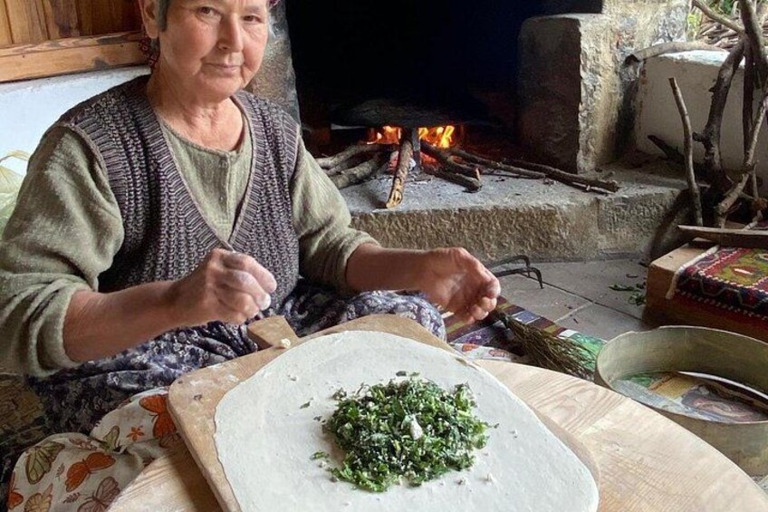 An elderly person preparing food outdoors with a fire in the background. 1