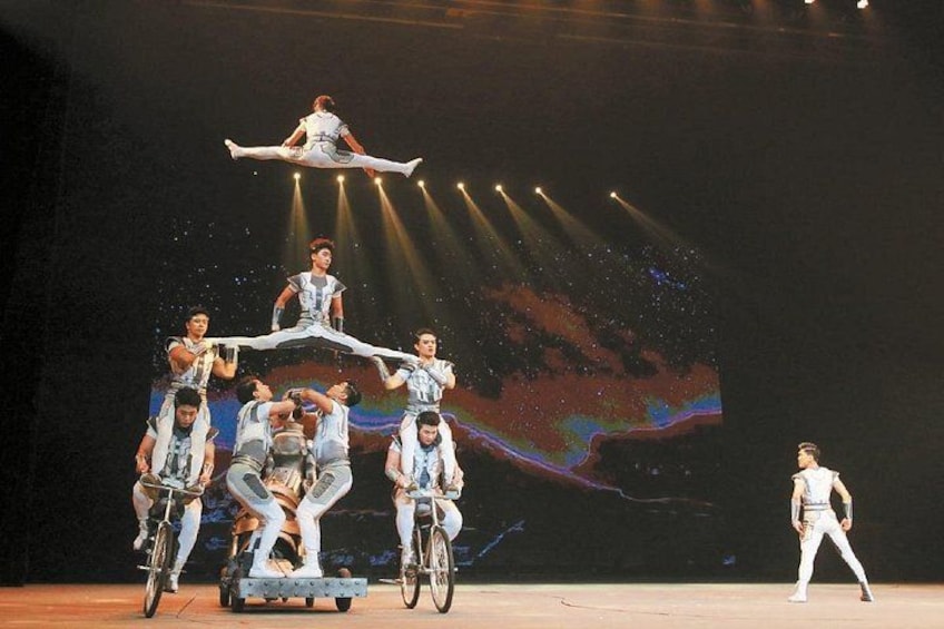 A group of performers on bicycles in a circus act, with a large screen displaying abstract visuals in the background. 5