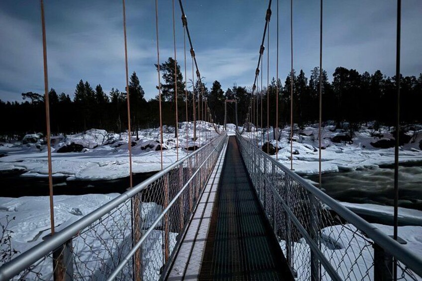 En hængebro over en flod med sne på bredderne og træer i baggrunden. 4