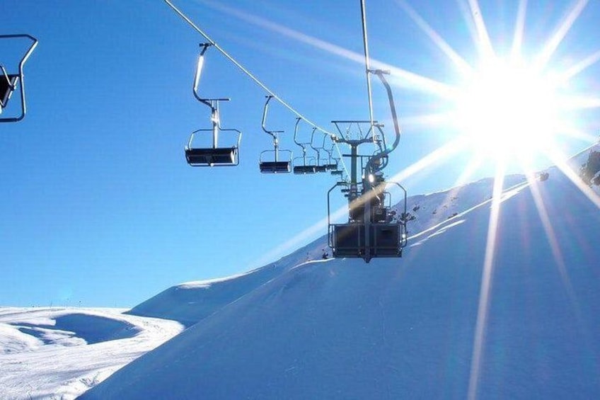 Een stoeltjeslift beklimt een besneeuwde helling onder een heldere lucht. 1