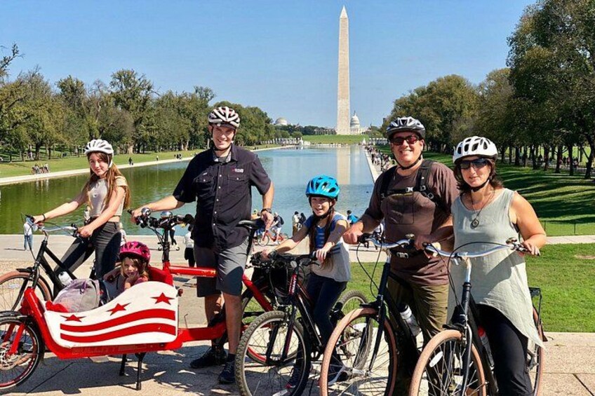 Un gruppo di persone in bicicletta con il Monumento a Washington sullo sfondo. 1