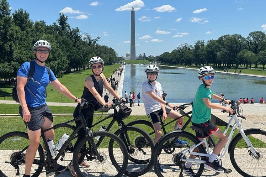 Quattro persone in bicicletta vicino a un grande monumento e a un corso d'acqua. 3