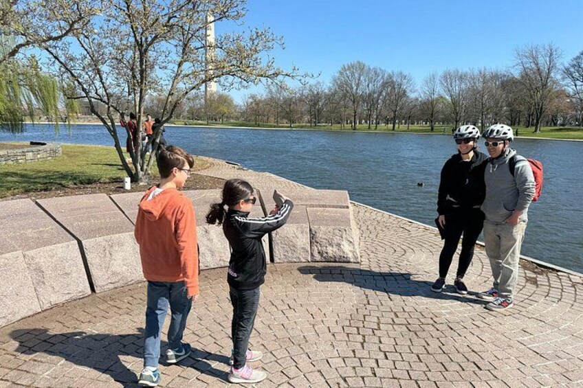 Un gruppo di persone vicino all'acqua, con una passeggiata lastricata e alberi sullo sfondo. 2