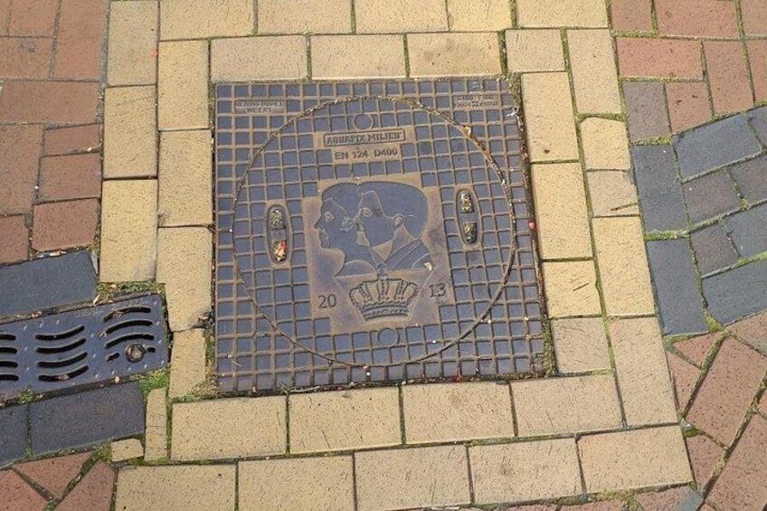 A manhole cover with a commemorative plaque, a metal grate, and a brick pavement. 3