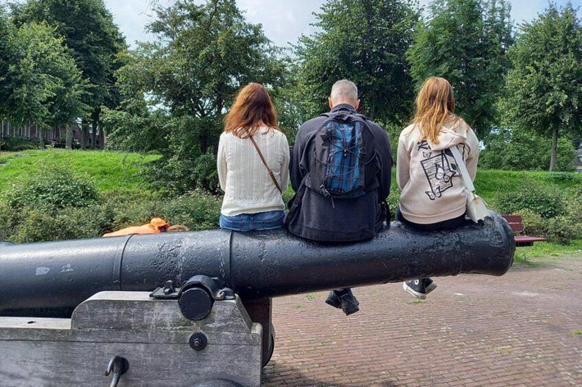 Three people sitting on a cannon in a park. 4